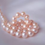 白いシーツの上にピンク色の輝く真珠が巻かれている