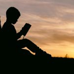 夕日が差し込む木陰で読書をする少年の写真