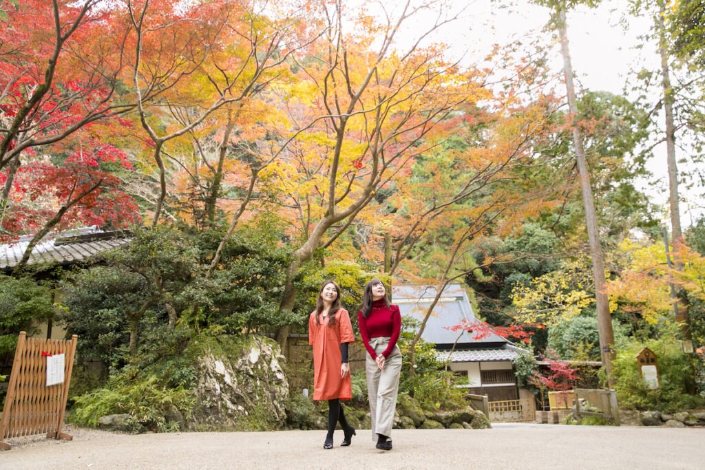 紅葉が美しい箕面公園内を女性二人が並んで歩いている様子。