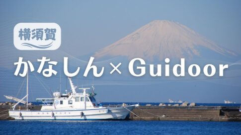 港に停泊している白い船と静かな青い海、背景には晴れた空の下、雪をかぶった富士山が見えます。画像には横浜と、かなしん×Guidoorの文字が白字で書かれています。